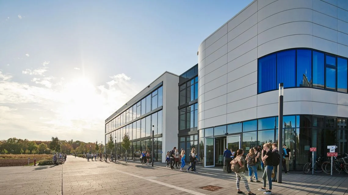 Außenansicht des Hörsaalzentrums der Universität Bonn mit modernen Glas- und Metallfassaden, Studierende gehen auf dem Vorplatz bei Sonnenschein.